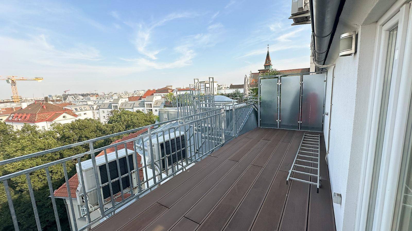 Langer Balkon mit Holzboden, Metallgeländer und Stadtblick.