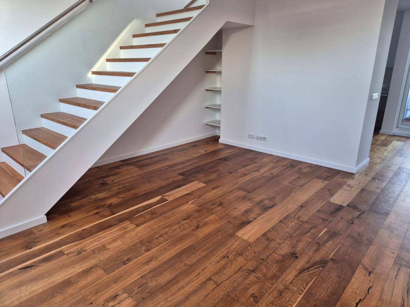 Heller Wohnbereich mit moderner Holztreppe und integrierten Regalen.