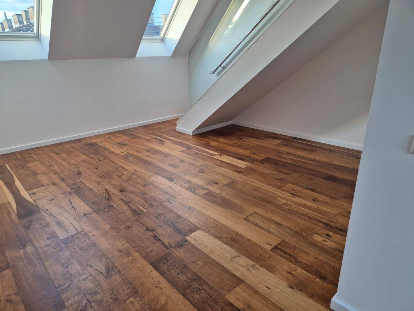 Geräumiger Wohnbereich mit Holzboden, schrägen Wänden und hellen Dachfenstern.