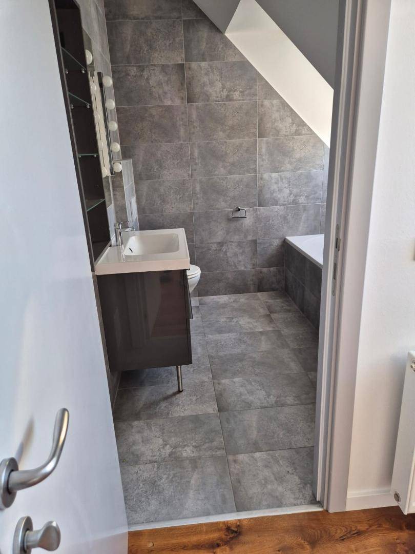 Modernes Badezimmer mit Badewanne, Waschbecken und grauen Fliesen unter Dachschräge.