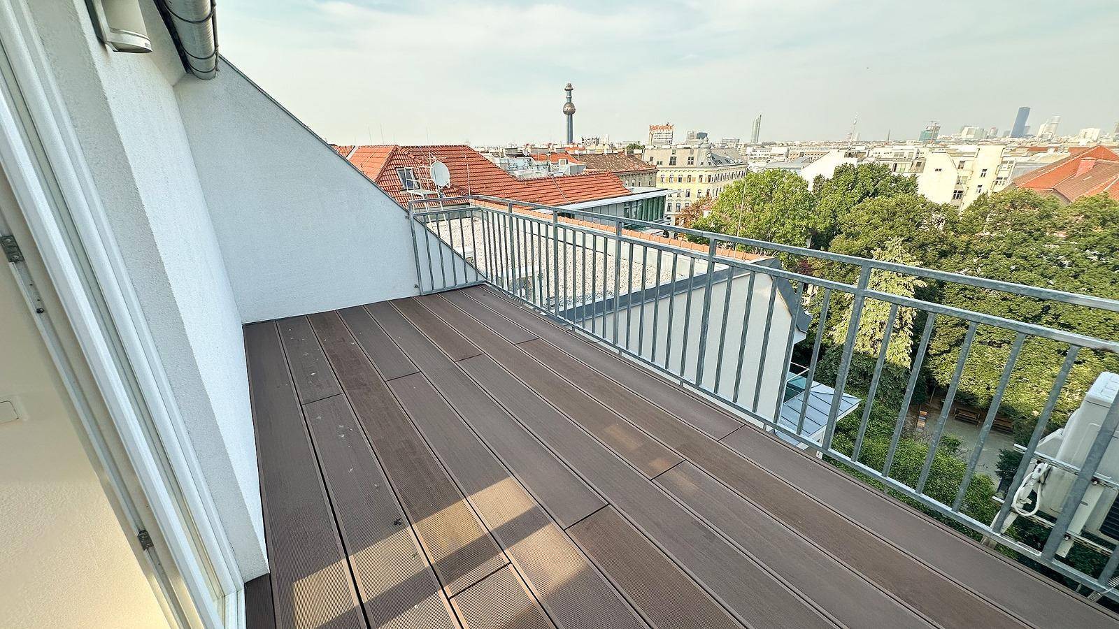 Geräumiger Balkon mit Holzboden und Blick auf die Stadt.