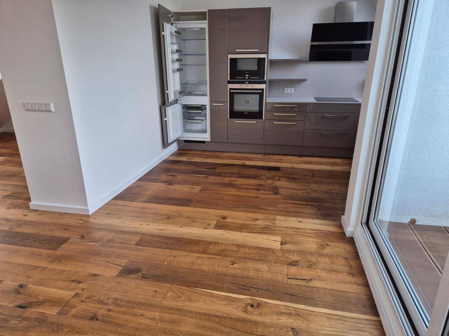 Moderne Einbauküche mit integriertem Kühlschrank und Holzboden.