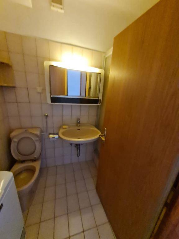 Badezimmer mit beigefarbener Toilette, Waschbecken und Spiegelschrank, typisch für die 80er Jahre.