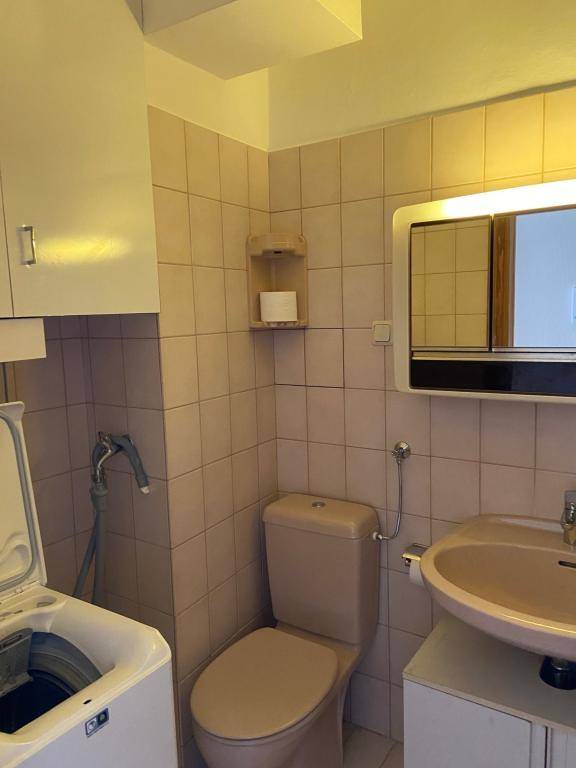 Funktionales Badezimmer mit beigefarbenen Fliesen, Toilette, Waschbecken und integrierter Waschmaschine.