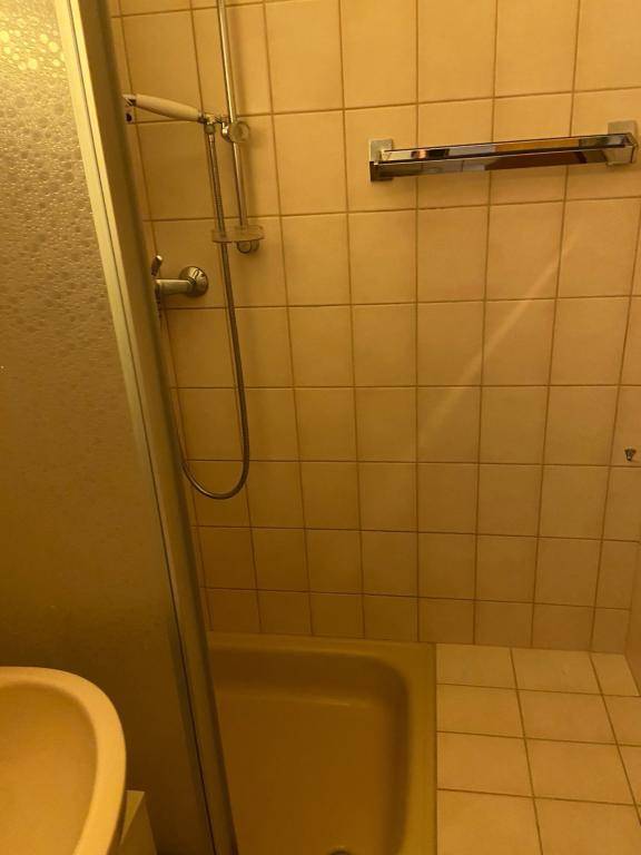 Innenansicht einer Duschkabine mit beigefarbenen Fliesen und einfacher Duscharmatur.