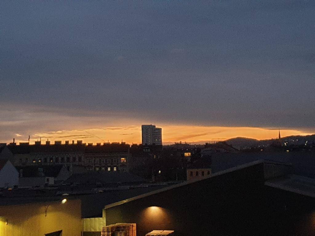 Städtische Skyline bei Sonnenuntergang mit warmen Farben am Horizont und dunklen Gebäudesilhouetten.