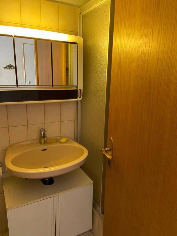 Waschbecken mit Spiegelschrank und beigefarbenen Fliesen in einem Badezimmer im Stil der 80er Jahre.