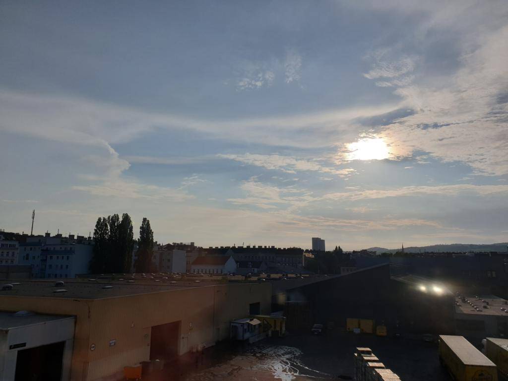 Städtische Ansicht bei Tageslicht mit bewölktem Himmel und der Sonne, die durch die Wolken bricht.