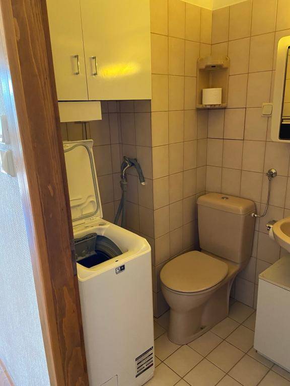 Badezimmer mit Waschmaschine, Toilette und beigefarbenen Fliesen, funktional eingerichtet.