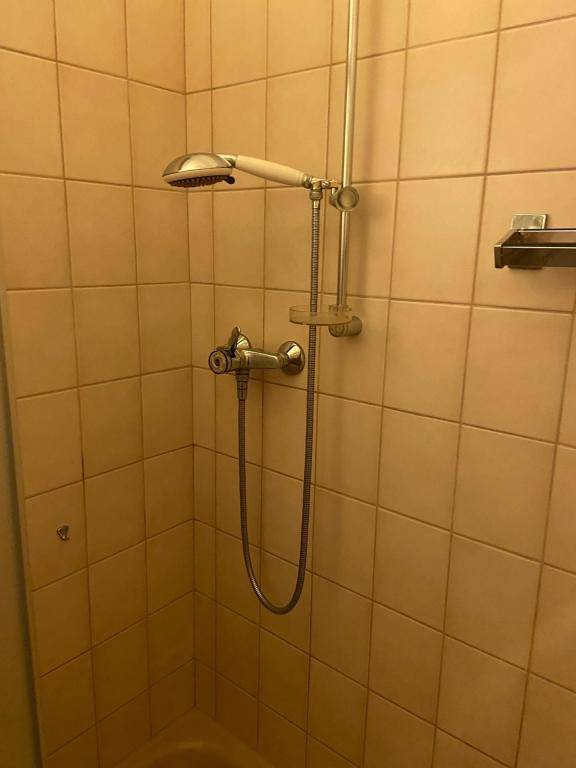 Duschkopf und Armatur an einer Wand mit beigefarbenen Fliesen in der Duschkabine.
