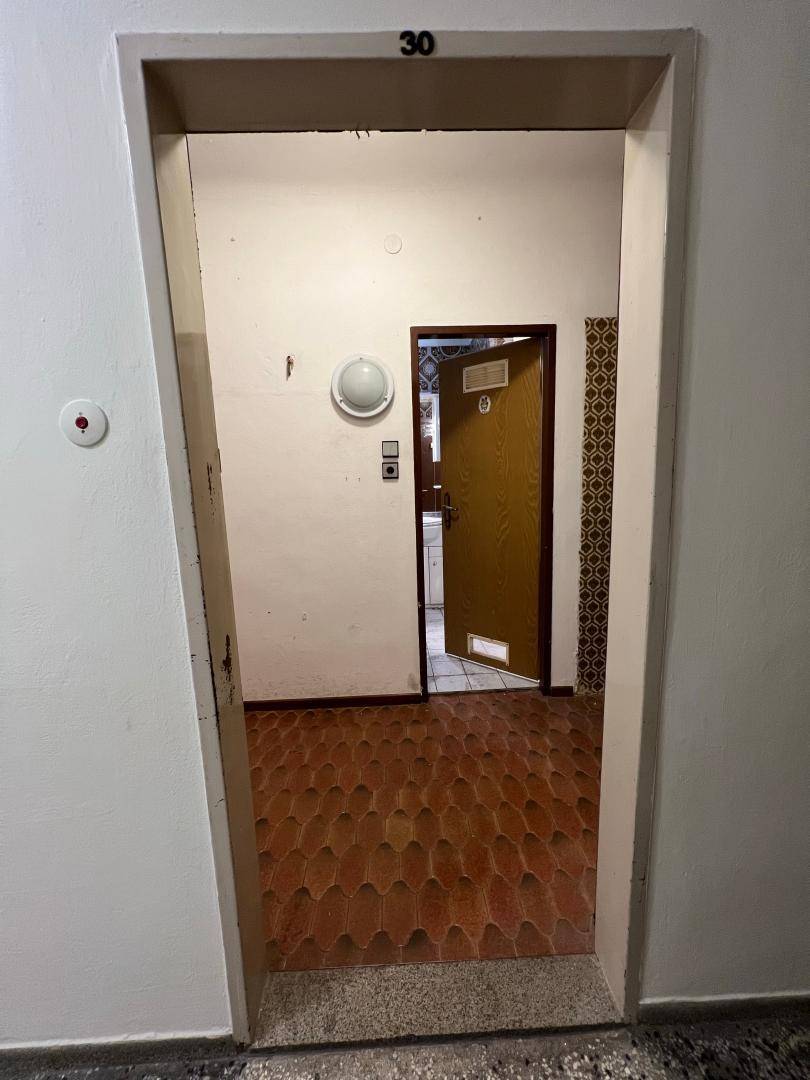 Eingangsbereich eines Flurs mit der Nummer 30 über dem Türrahmen und gemusterten Bodenfliesen.