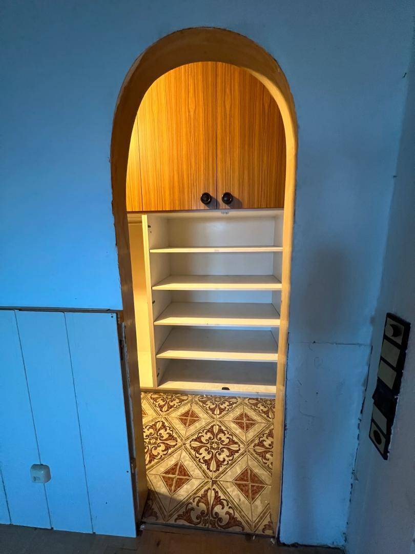 Eingebautes Regal in einer gewölbten Nische mit gemusterten Bodenfliesen und einem oberen Schrank.