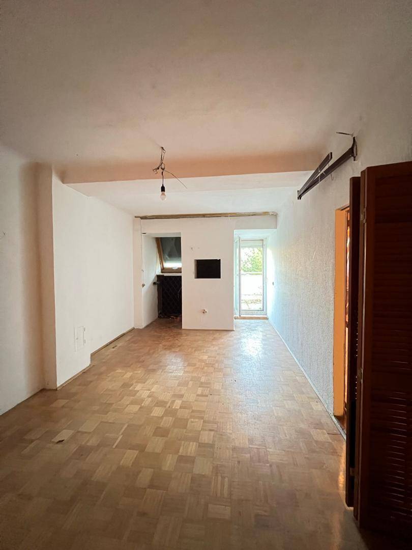 Geräumiger, leerer Raum mit Parkettboden, weißen Wänden und einem Fensterbereich mit integrierten Schränken.