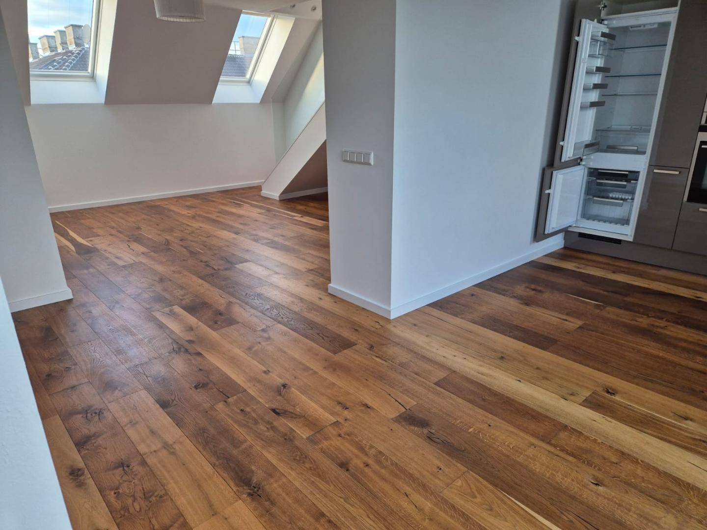 Offener Wohnbereich mit Holzboden, Dachschrägen und integrierter Küche.