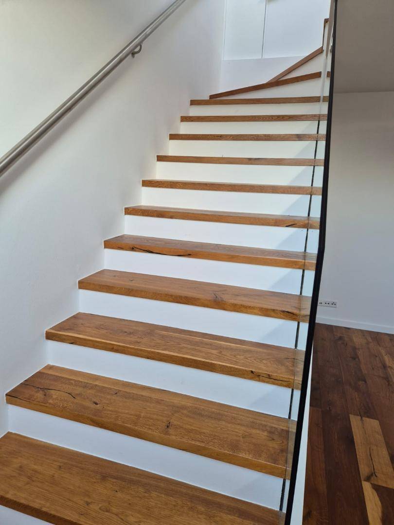 Moderne Holztreppe mit weiß gestrichenen Setzstufen und Glasgeländer.