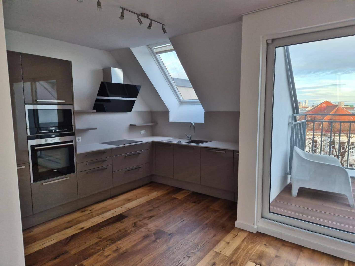 Helle Küche im Dachgeschoss mit Schrägdachfenster und Zugang zu einem kleinen Balkon.