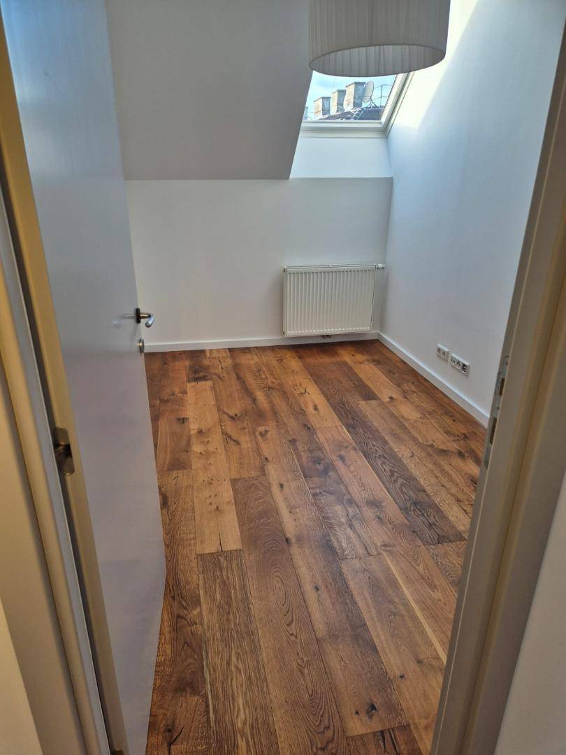 Helles Zimmer im Dachgeschoss mit Holzboden, Heizkörper und Dachfenster.
