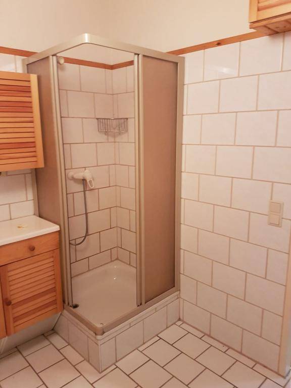 Badezimmer mit weiß gefliesten Wänden, Eckduschkabine und Holzschrank.