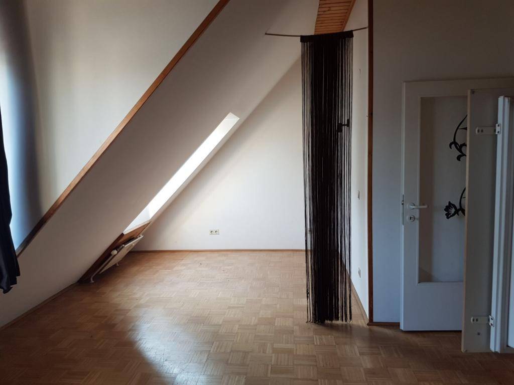 Heller Raum im Dachgeschoss mit Parkettboden, Schrägdach und Dachfenster.