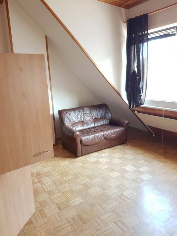 Gemütliches Wohnzimmer im Dachgeschoss mit Schrägdach, Parkettboden und Ledersofa.
