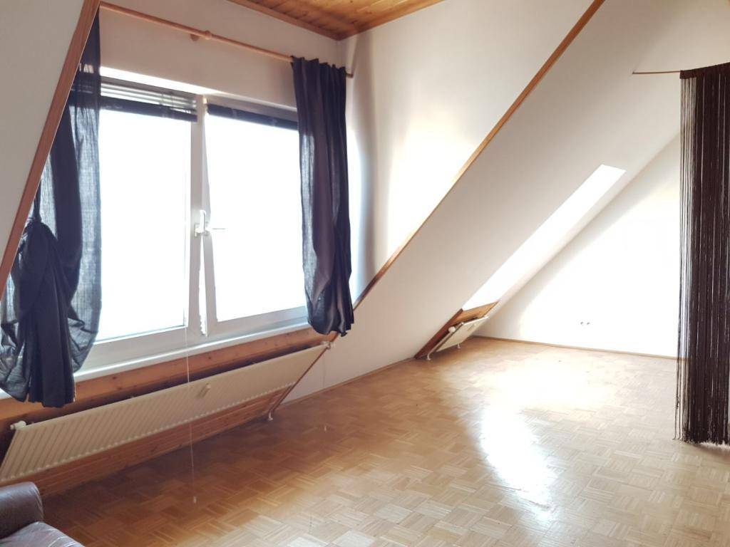 Heller Raum mit Dachschräge, Parkettboden und großem Fenster.