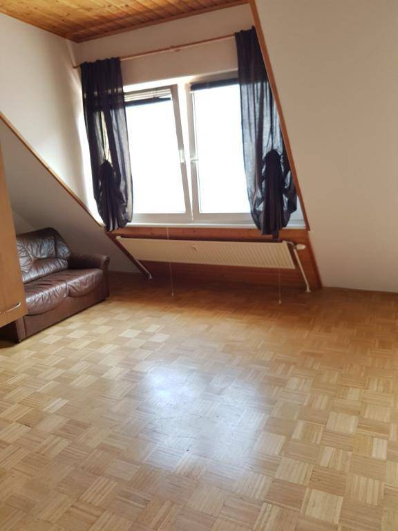 Helles Wohnzimmer mit Dachschräge, Parkettboden und großem Fenster.