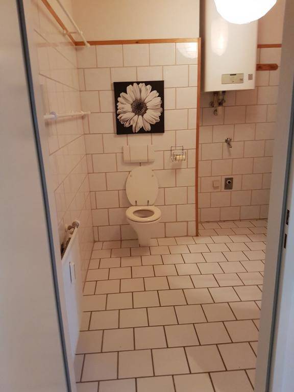 Badezimmer mit weißen Fliesen, Toilette und Warmwasserboiler an der Wand.