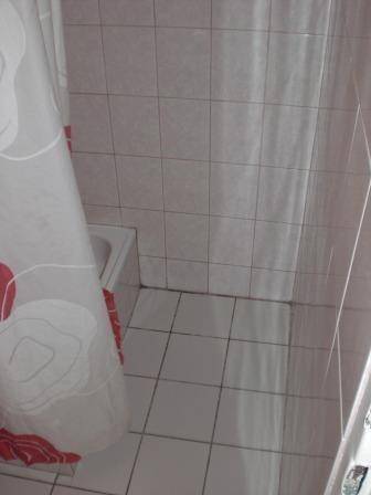 Duschbereich im Badezimmer mit Fliesenboden und Duschvorhang.