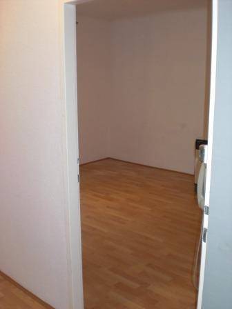 Blick in einen leeren Raum mit Holzfußboden und weißen Wänden.