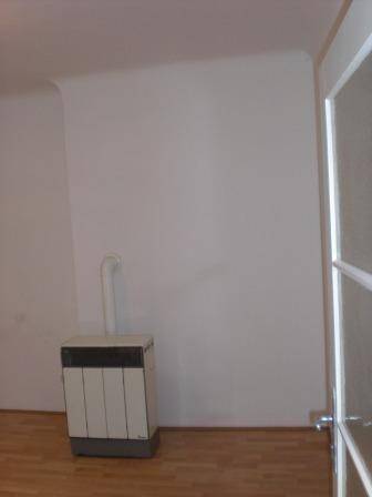 Heller Raum mit Holzfußboden und einem freistehenden Ofen an der Wand.