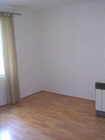 Leerer Raum mit Holzfußboden, weißen Wänden und einem Heizofen.