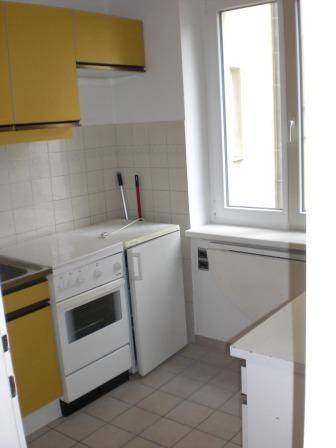 Küche mit Fliesenboden, Fenster, Herd und gelben Oberschränken.