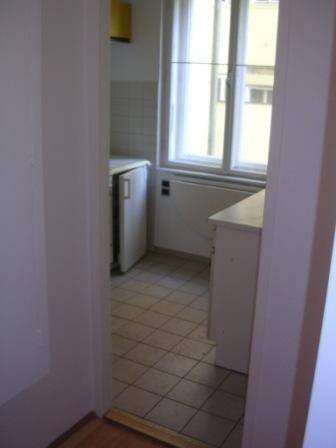 Eingang zur Küche mit Fliesenboden, Fenster und einfachen Küchenschränken.
