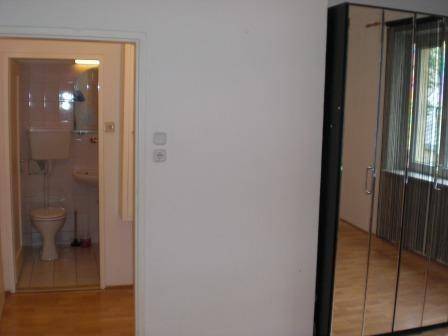 Flur mit Holzfußboden und Zugang zu einem Badezimmer mit WC und Waschbecken.