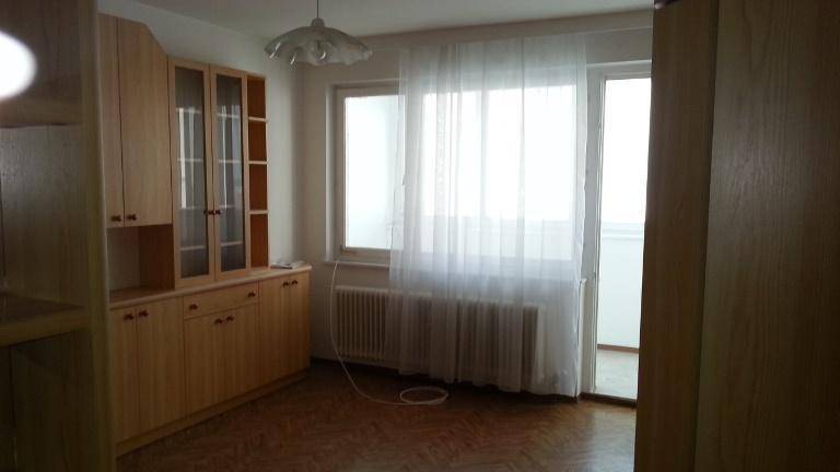 Helles Wohnzimmer mit großem Fenster, Heizkörper und einer Holzschrankwand, die viel Stauraum bietet.