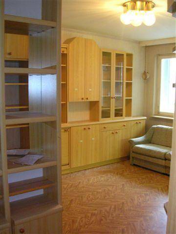 Gemütliches Wohnzimmer mit Holzparkettboden, großer Holzschrankwand und einem bequemen Sessel.
