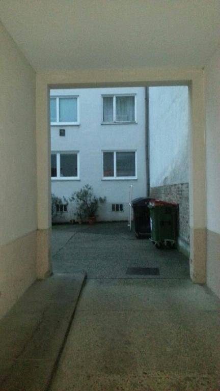 Blick durch einen Durchgang auf einen Innenhof mit Gebäudefassade und Mülltonnen, inklusive einer Rampe.