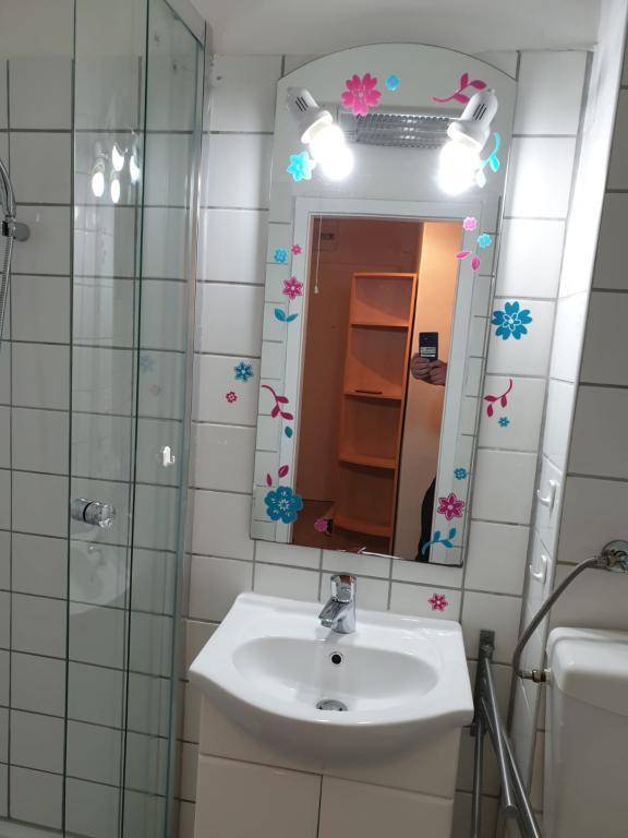 Badezimmer mit Waschbecken, beleuchtetem Spiegel und Duschkabine, der Spiegel ist floral verziert.