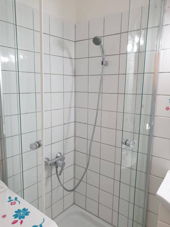 Badezimmer mit einer Eckduschkabine, weißen Fliesen und einer einfachen Duscharmatur.