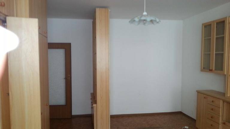 Heller Raum mit weißer Wand, Holztrennwand und einer Tür, die zu einem weiteren Bereich führt.