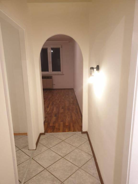 Flur mit Fliesenboden, der durch einen Bogen in einen Raum mit Holzfußboden und Fenster führt.