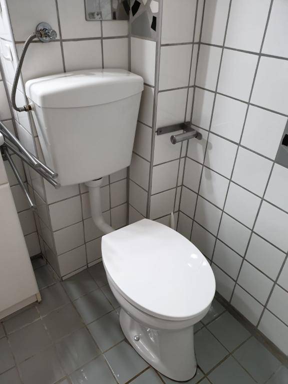 Toilette mit einem hoch angebrachten Spülkasten und weißen Wandfliesen, in einem einfachen Badezimmer.