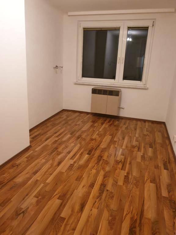 Leerer Raum mit Laminatboden, weißen Wänden und einem Fenster mit Heizkörper darunter.