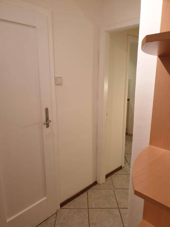 Flur mit Fliesenboden, weißen Wänden und einem Holzregal, das einen einfachen und funktionalen Stil zeigt.