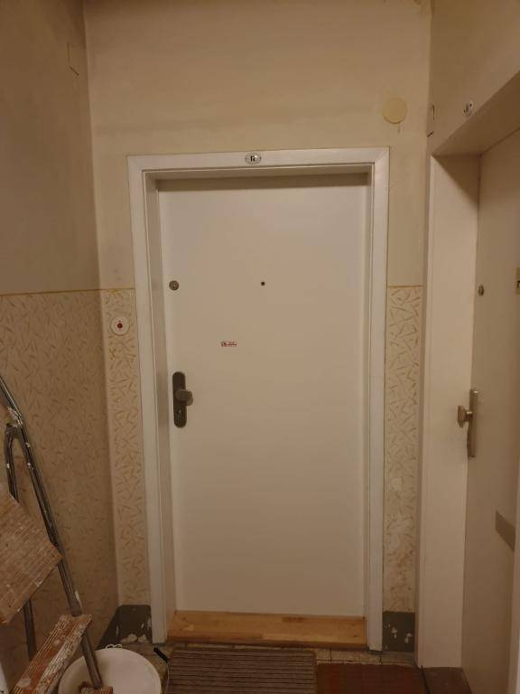 Weiße Wohnungseingangstür in einem Flur mit älterer Tapete und einfacher Ausstattung.