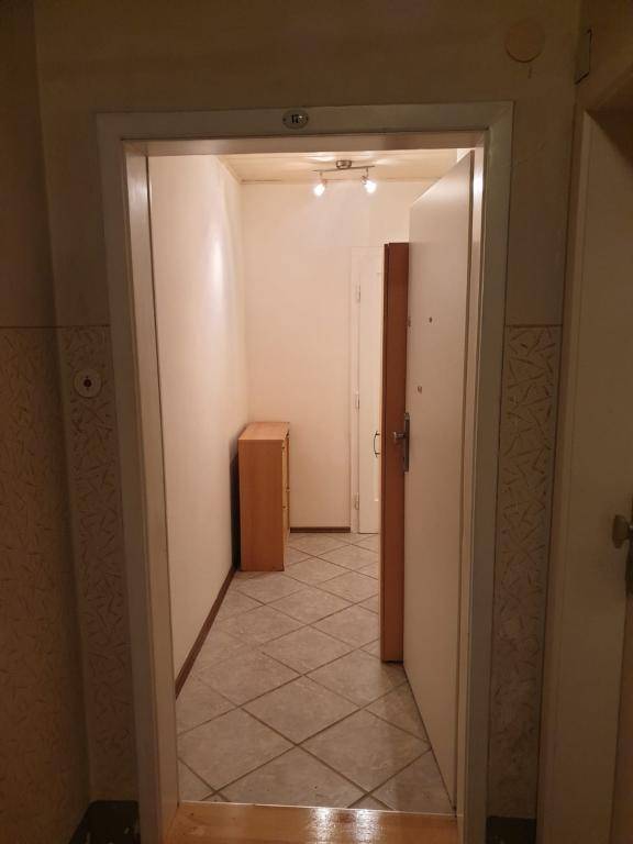 Blick vom Eingang in einen Flur mit Fliesenboden, einem kleinen Holzschrank und Durchgang zu weiteren Räumen.