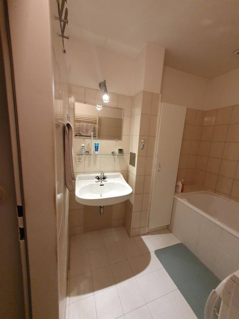 Badezimmer mit Waschbecken, Spiegel und beigen Wandfliesen.