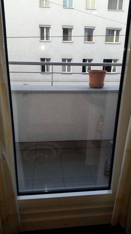 Blick von einem Balkon mit Fliesenboden und Geländer auf ein gegenüberliegendes Gebäude.