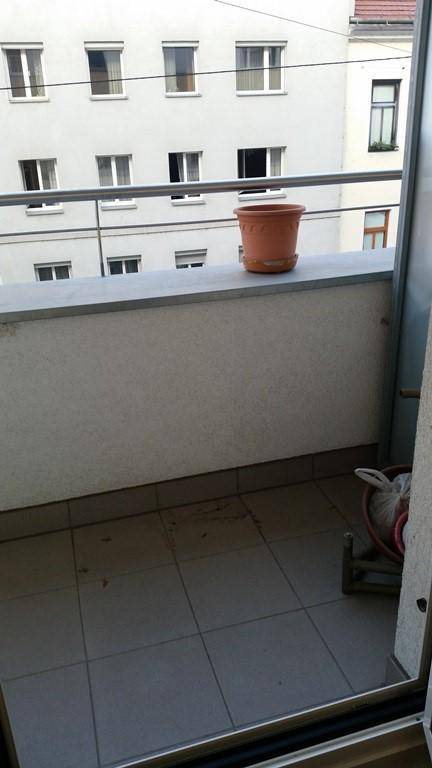 Kleiner Balkon mit Fliesenboden und einem Blumentopf, mit Blick auf die Nachbarschaft.