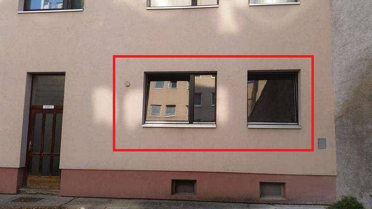 Nahaufnahme der hellen Fassade mit zwei Fenstern im Erdgeschossbereich des Gebäudes.